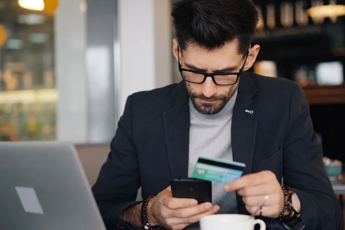 A man checking his credit score on his phone next to a laptop before applying to buy a car