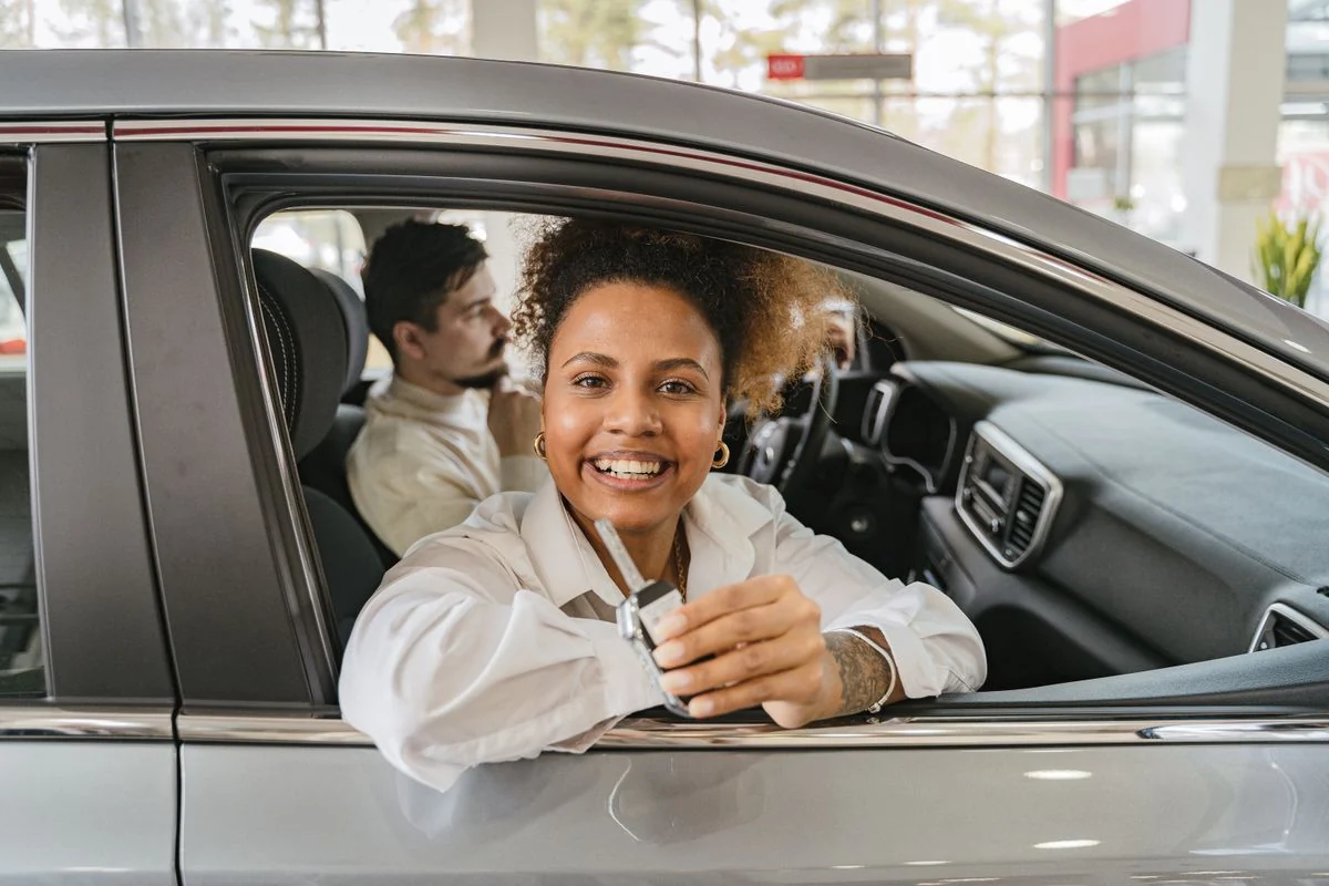A happy first-time buyer holding up the keys to a newly financed car at the dealership