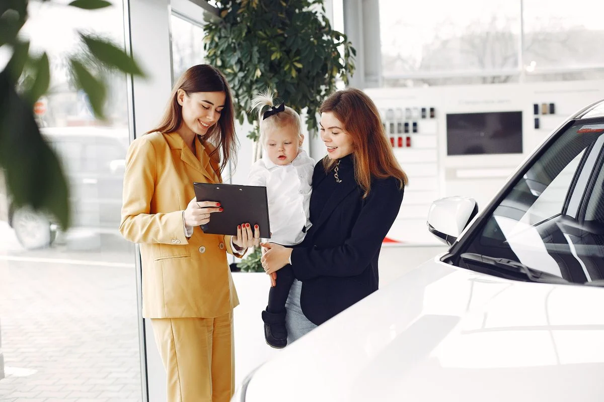 A mother and child looking at paperwork with a saleswoman while choosing their first financed family car in a showroom