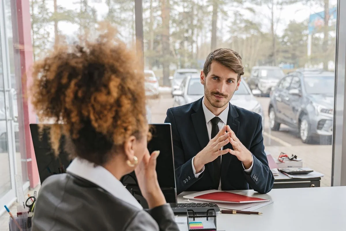 A first-time car buyer talking through no-credit financing options across the desk with a dealership finance manager