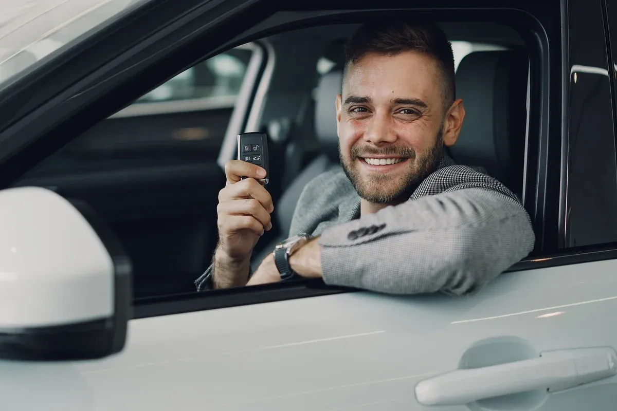 A first-time car buyer sitting in the driver's seat of a used car holding the keys after completing the purchase