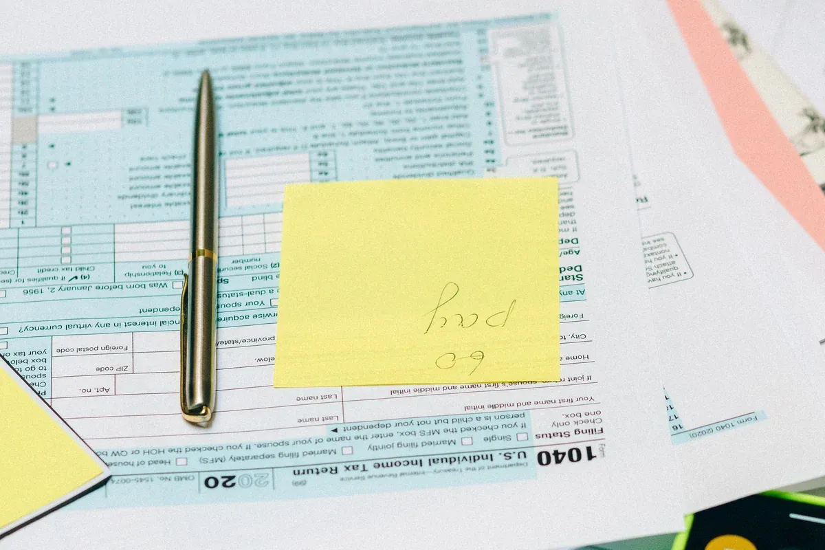 Income tax forms, a pen, a calculator and reading glasses laid out on a desk while preparing a car loan application