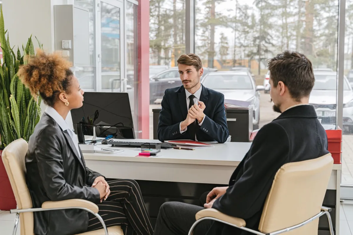 A buyer reviewing car financing options and paperwork with a dealership finance manager at a desk