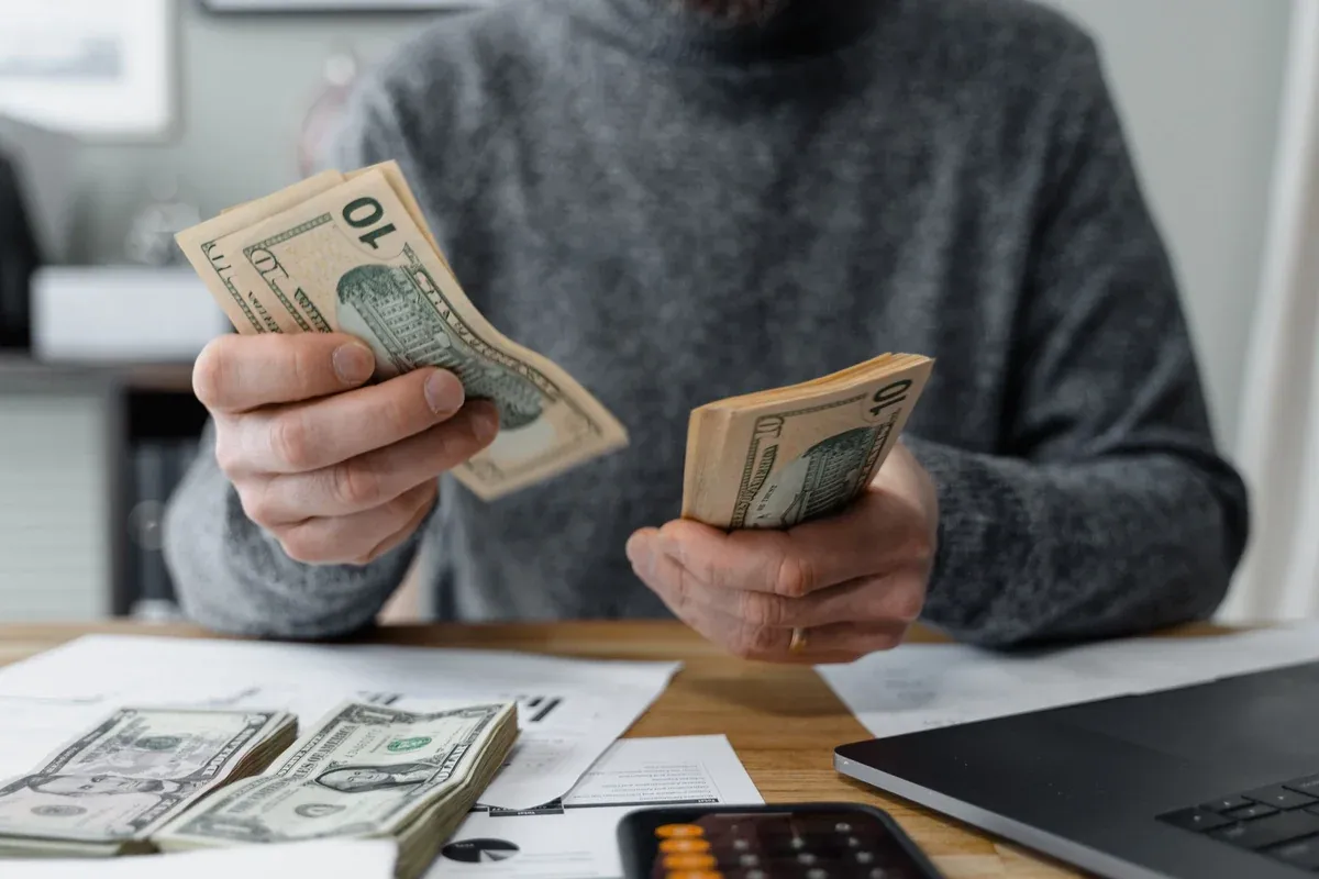 Close-up of a buyer counting out cash for a car down payment at a desk with loan paperwork and a calculator