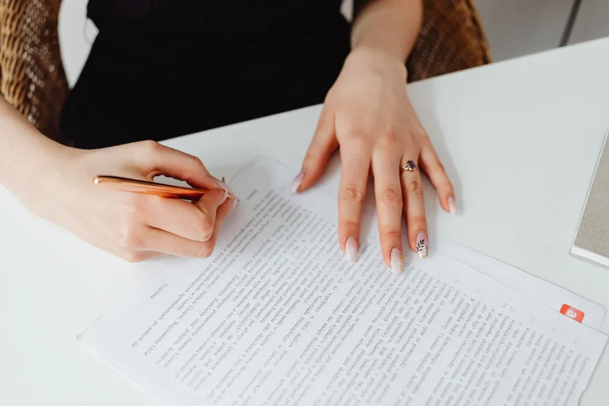 Close-up of one person's hands signing a finance agreement at a desk, holding the page steady with a pen in hand