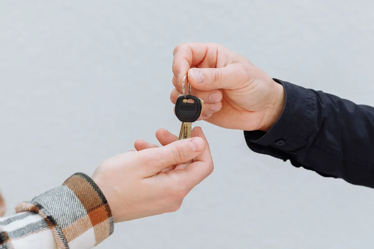 Two hands exchanging a car key over a signed document while trading in a vehicle at a dealership