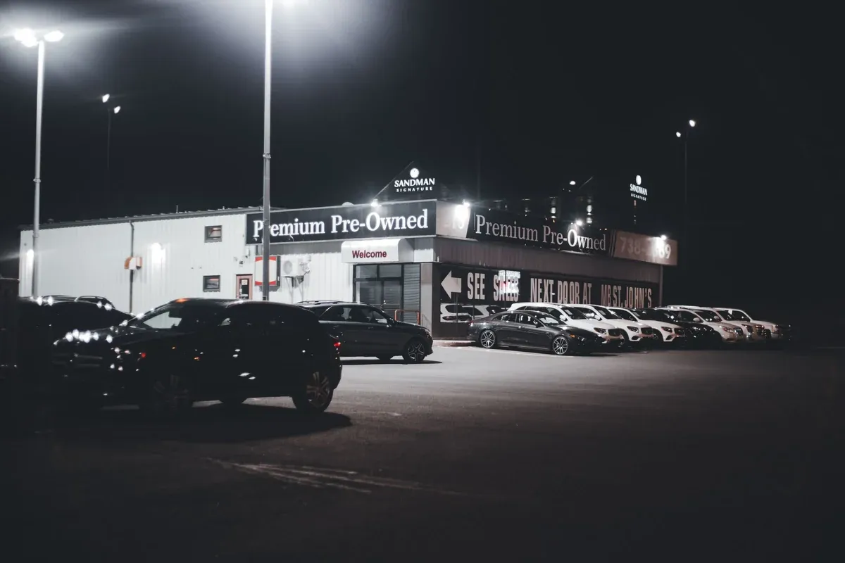 A used car dealership lot at dusk with rows of pre-owned vehicles under the lot lights and a Premium Pre-Owned sign