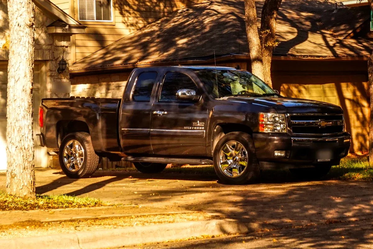 A dark grey used Chevrolet Silverado extended-cab pickup parked in a suburban driveway in the late afternoon
